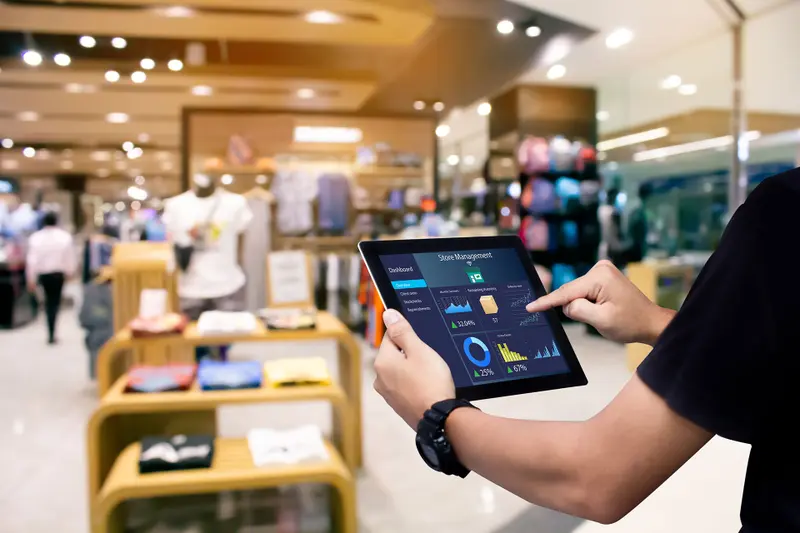 A store manager checks a stock dashboard on a tablet in a clothing store
